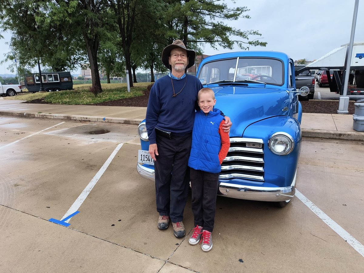 Adult and child in blue clothing standing in front of the vintage blue 1953 Chevy pickup that gave Little Blue's Farm its name at the Peoria Riverfront Farmers Market.