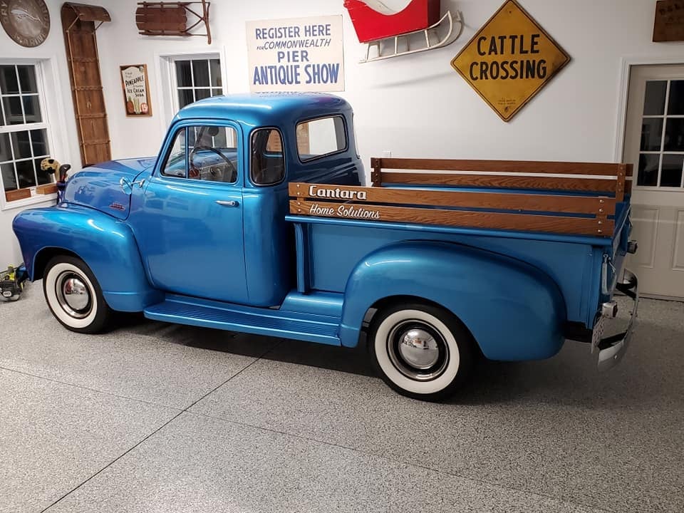 Blue vintage pickup truck with wood bed parked in front of antique shop signs and building